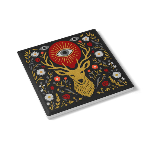 Square ceramic coaster, 4x4 inches, with cork backing. Charcoal tile showcases a golden stag head with antlers, surrounded by florals and an all-seeing eye in red and gold. Smooth printed surface; bold folk-art style. Witchy occult deer coaster for dark academia décor, bar cart, or living room. Square ceramic drink coaster with cork base, stag and eye design.